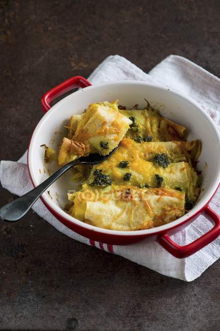Crespelle with leek and basil pesto in red pot over towel — Stock Photo