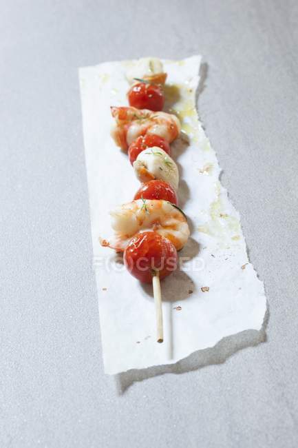 Ein Garnelen- und Tomatenspieß auf Papier über grauer Oberfläche — Stockfoto