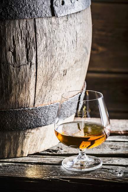 Glass of cognac next to old wooden barrel — Stock Photo