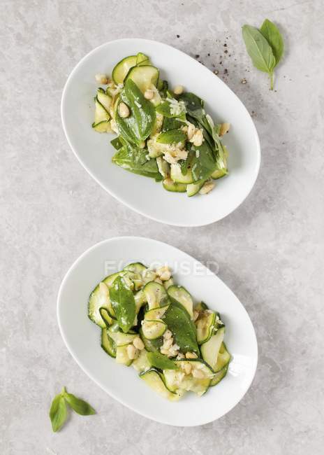 Zucchini mit Basilikum und Pinienkernen auf weißen Tellern — Stockfoto
