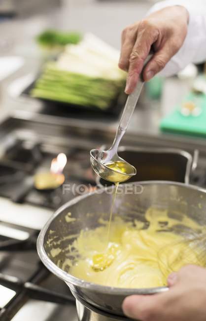 Vista ritagliata delle mani che aggiungono olio alla salsa di Bechamel con mestolo — Foto stock