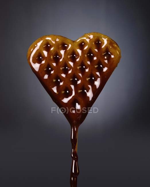 Крупный план веганских вафель в форме сердца на палочке, смоченной в кленовом сиропе — стоковое фото
