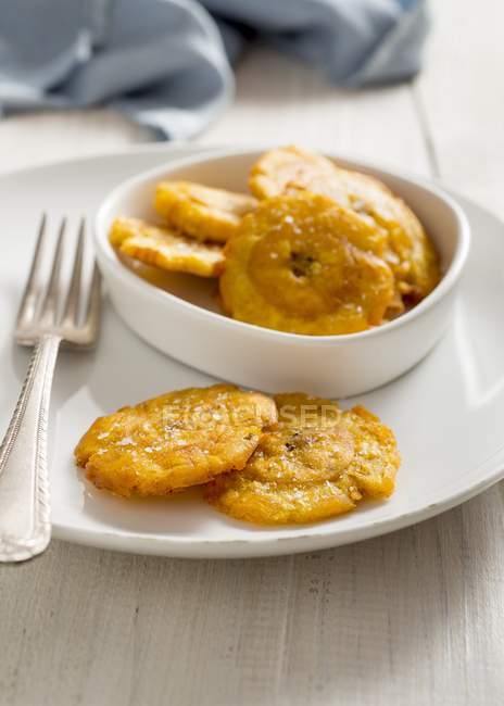 Vue rapprochée des patacones frits colombiens avec fourchette sur des plats blancs — Photo de stock