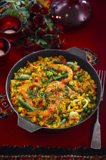 Paella with prawns in black pan over red surface — Stock Photo