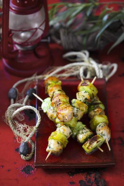 Brochettes de pétoncles et de concombre grillées sur plaque sur surface rouge — Photo de stock