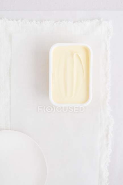 Vista superior de una tina de plástico de margarina sobre un paño blanco - foto de stock
