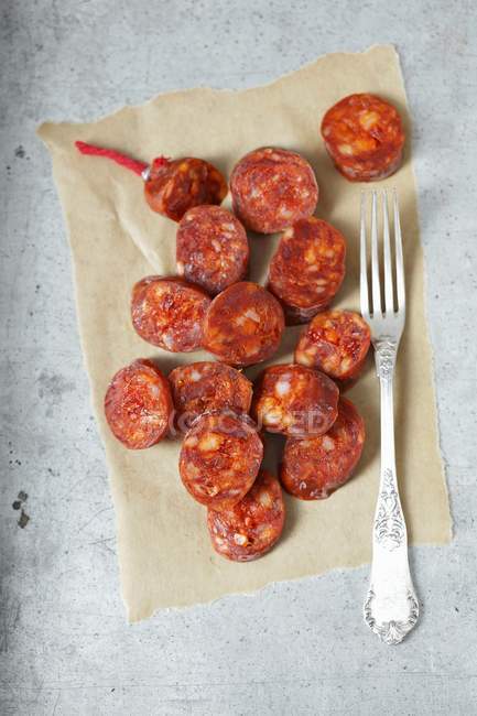 Top view of Chorizo slices on a piece of paper with a fork — Stock Photo