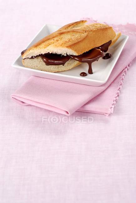Closeup view of baguette with chocolate sauce on square plate and pink towel — Stock Photo