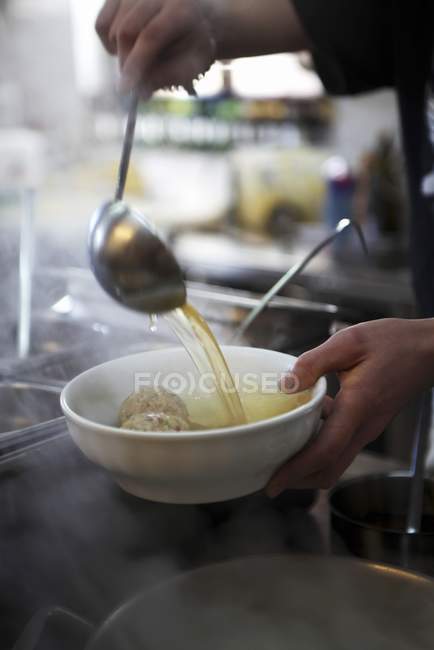Обрезанный вид рук, полных клецки супа в миску — стоковое фото