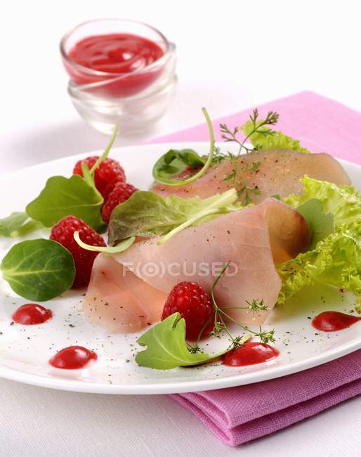 Closeup view of swordfish Carpaccio with raspberries, sauce and leaves — Stock Photo