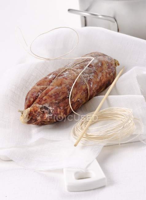 Closeup view of Cotechino sausage with string on white cloth — Stock Photo