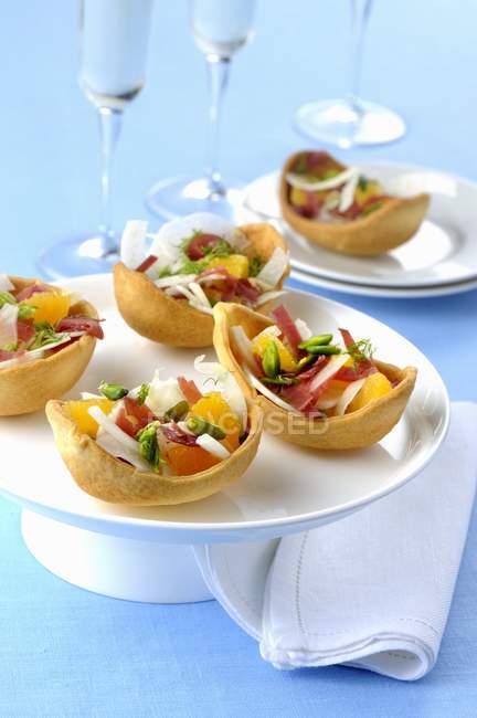 Conchas de pastelería rellenas de jamón, pomelo y verduras en plato blanco sobre superficie azul - foto de stock