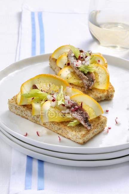 Crostini con anchoas y naranjas en plato blanco - foto de stock
