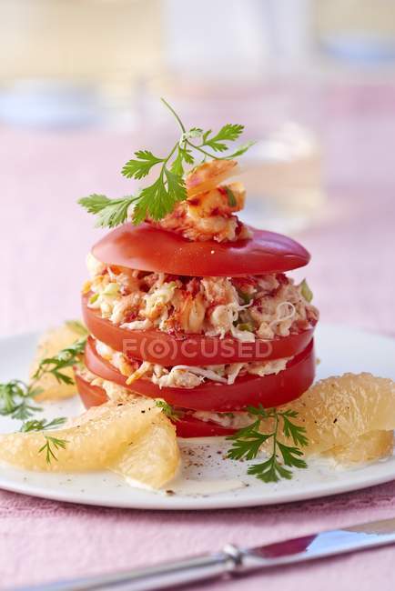 Ein Tomatenturm mit Grapefruit und Krabbenfleisch auf weißem Teller über rosa Oberfläche — Stockfoto