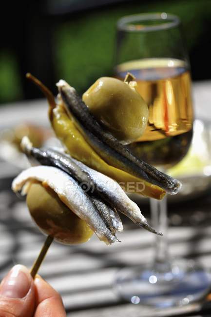 A hand holding an anchovy, green olive and chilli pepper kebab — Stock Photo