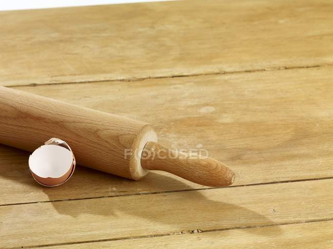 Closeup view of a rolling pin and an eggshell on a wooden surface — Stock Photo