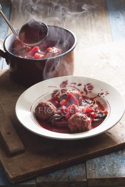 Steaming beetroot soup with meat dumplings  on white plate over wooden desk — Stock Photo