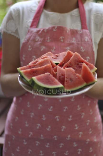 Una donna che indossa un grembiule con un piatto di fette di melone, sezione centrale — Foto stock