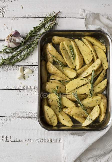 Pommes de terre romarin prêtes à rôtir dans un plat sur une surface en bois — Photo de stock
