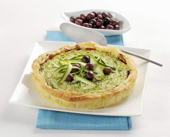 Courgette tart with olives  on white plate  over towel — Stock Photo