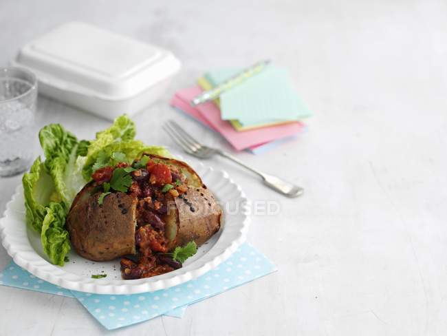 A jacket potato with chilli on white plate over towel — Stock Photo