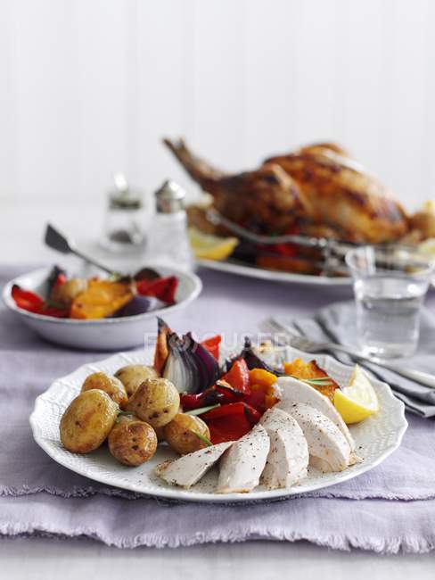 Grilled chicken with potatoes and a pepper medley  on white plate over tablecloth — Stock Photo