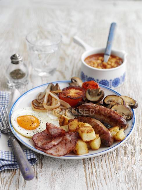 Una classica colazione all'inglese su piatto bianco su superficie in legno con forchetta — Foto stock