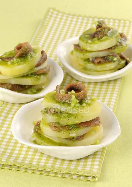 Batata mille feuilles com anchovas e molho de ervas em pratos brancos sobre toalha — Fotografia de Stock