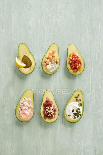 Avocados mit verschiedenen Füllungen über grüner Holzoberfläche — Stockfoto