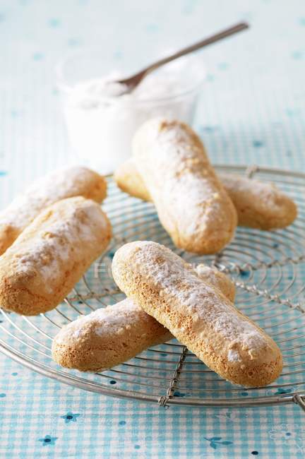 Closeup view of sponge fingers with icing sugar on a wire rack — Stock Photo