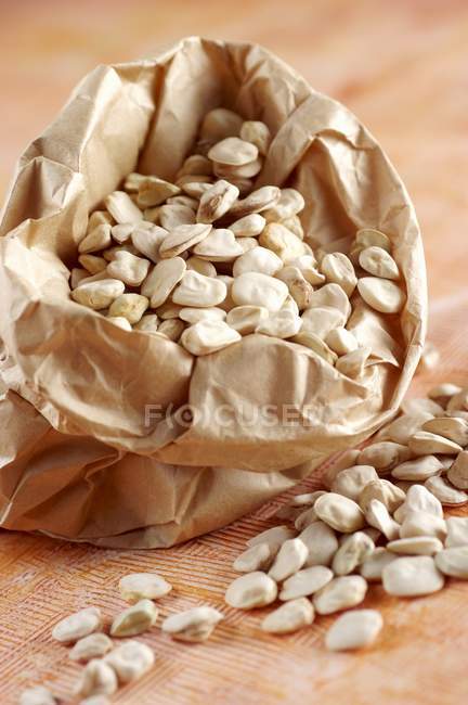 Cicerchie - chickling vetches in paper bag and scattered on wooden surface — Stock Photo