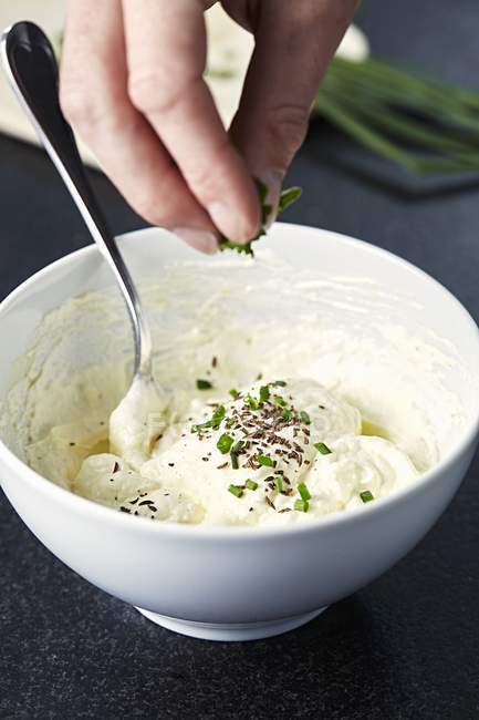 Hand sprinkling quark and flaxseed oil spread with herbs — Stock Photo