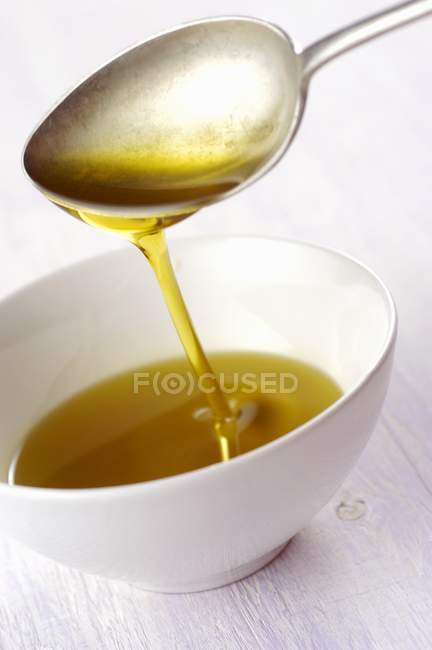 Vue rapprochée de l'huile qui coule d'une cuillère à un bol — Photo de stock