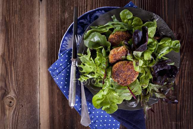 Quinoa fritters on a bed of lettuce on plate with fork and knife  over wooden surface — Stock Photo