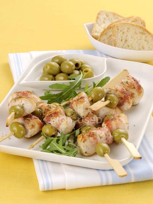 Chicken and bacon kebabs with green olives  on white plate over towel — Stock Photo
