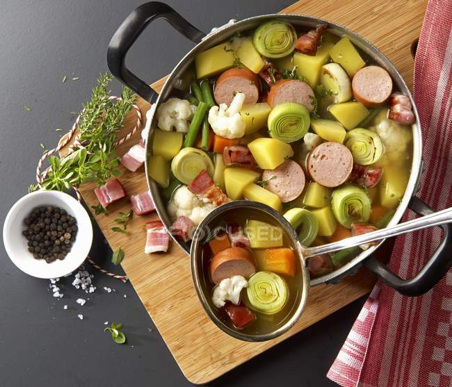 Рагу из овощей с колбасой и беконом на кастрюле над деревянным столом — стоковое фото