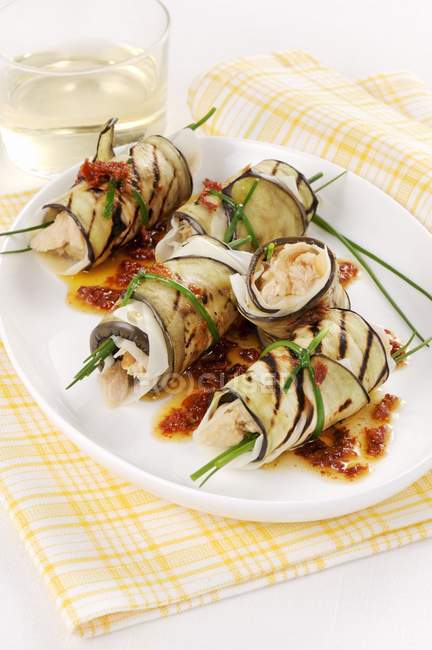 Aubergine rolls filled with fish in a tomato oil  on white plate  over towel — Stock Photo