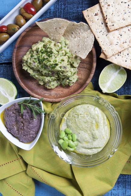 Three dips: guacamole, olive paste and pea cream in bowls over table — Stock Photo