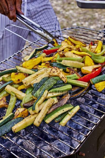 Légumes sur une grille de barbecue et vue recadrée de pinces dans les mains de l'homme — Photo de stock