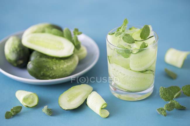 Water with cucumber strips, mint and ice on a blue surface — Stock Photo