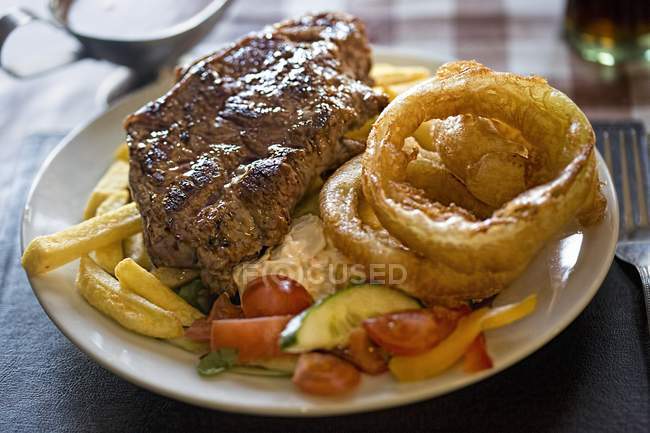Стейк с чипсами и салатом на тарелке — стоковое фото