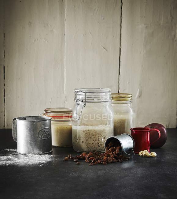 Still life with sour dough in jars, raisins, cashew nuts and apple — Stock Photo