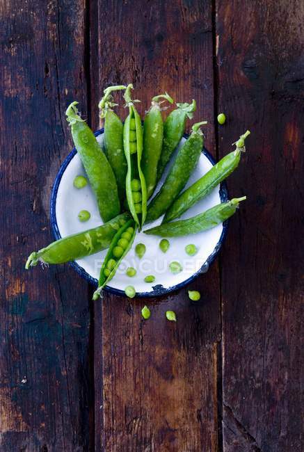 Freshly washed peapods in an enamel bowl over wooden surface — Stock Photo