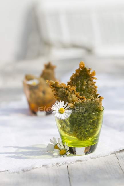 Beer-battered stinging nettle leaves in glass over cloth — Stock Photo
