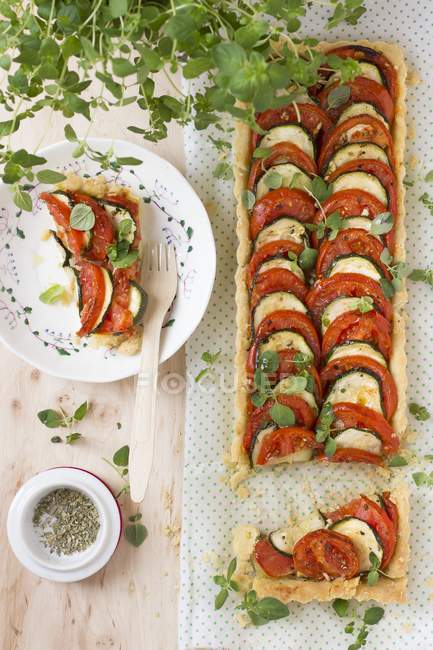Tomato and courgette tart with oregano over woden surface with towel — Stock Photo