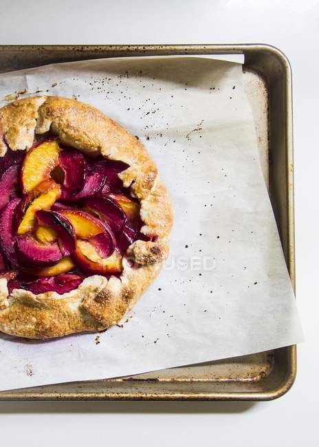 A galette with peaches and plums on tray with baking paper — Stock Photo