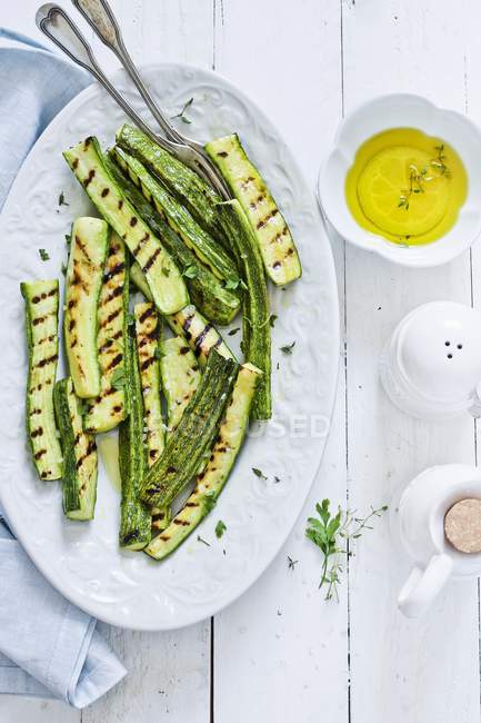 Gegrillte Zucchini und Olivenöl auf weißem Teller über Holzoberfläche — Stockfoto