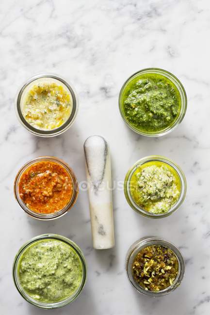 Top view of assorted jars of Pesto on a marble surface with a pestle — Stock Photo