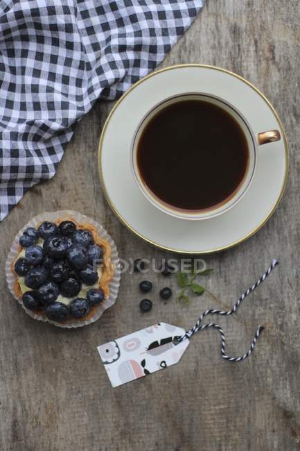 Closeup top view of cup of coffee and a blueberry tartlet — Stock Photo