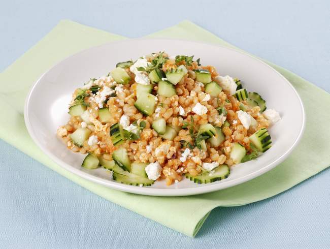 Pearl barley with tomato pesto and cucumber on white plate over towel — Stock Photo